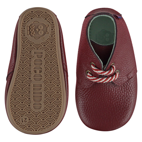 A pair of childrens lace up desert boots, one viewed from the top, one is a view of the sole. They are in red wine colour leather with striped laces. They have a  pale blue leather lining and insole. The sole is a natural gum colour.