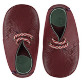 A pair of childrens lace up desert boots, both viewed from the top, facing in opposite directions. They are in red wine colour leather with striped laces. They have a  pale blue leather lining and insole. The sole is a natural gum colour.
