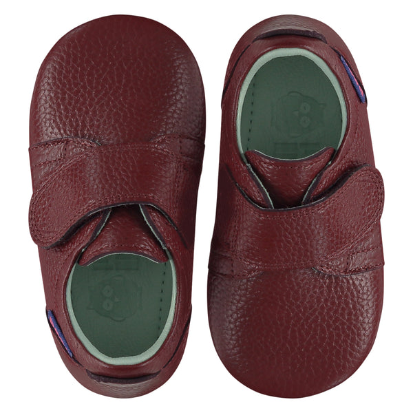 A pair of childrens adjustable strap shoes, viewed from the top. They are facing in opposite directions. They are in wine red leather with a large adjustable strap over the top of the foot. They have a  pale blue leather lining and insole. The sole is a natural gum colour.