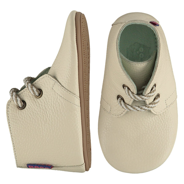 A pair of childrens lace up desert boots, one viewed from the top, one is a view of the side. They are in chalk colour leather with striped laces. They have a  pale blue leather lining and insole. The sole is a natural gum colour.