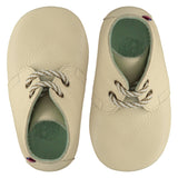 A pair of childrens lace up desert boots, both viewed from the top, facing in opposite directions. They are in chalk colour leather with striped laces. They have a  pale blue leather lining and insole. The sole is a natural gum colour.