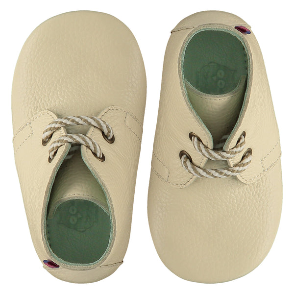 A pair of childrens lace up desert boots, both viewed from the top, facing in opposite directions. They are in chalk colour leather with striped laces. They have a  pale blue leather lining and insole. The sole is a natural gum colour.