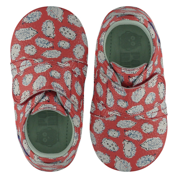 A pair of childrens adjustable strap shoes, viewed from the top. They are facing in opposite directions. They are in red leather with an all over print of hedgehogs. They have a  pale blue leather lining and insole. The sole is a natural gum colour.