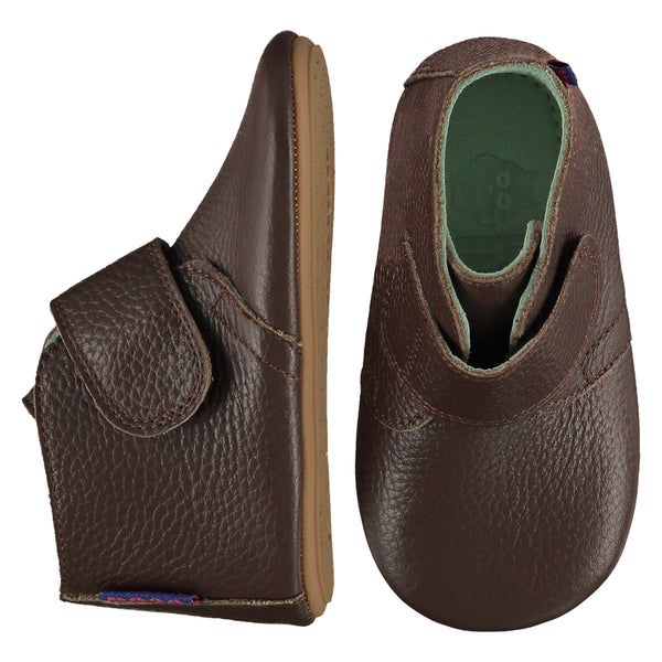 A pair of childrens adjustable strap ankle boots, one viewed from the top, one is a view from the side. They are in dark brown colour leather with a large adjustable strap over the foot. They have a  pale blue leather lining and insole. The sole is a natural gum colour.