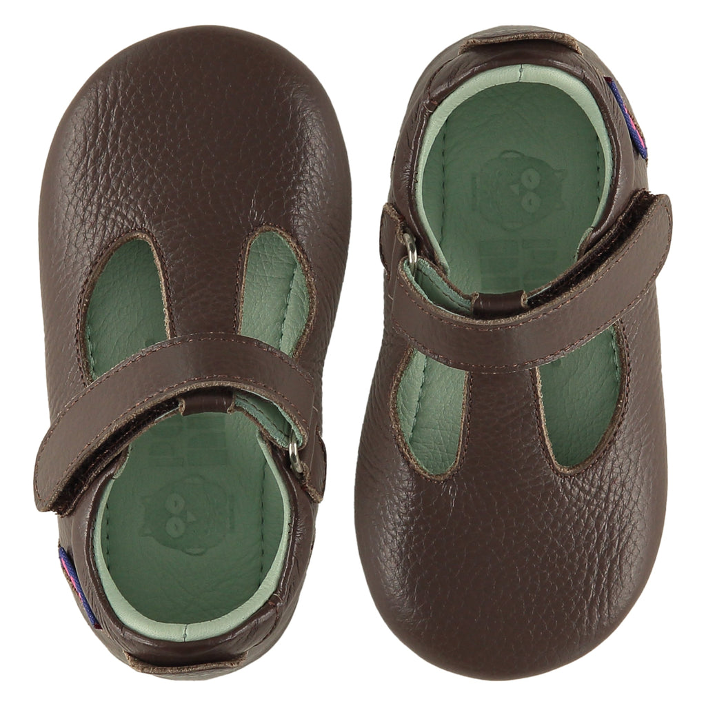 A pair of childrens T bar shoes, viewed from the top. They are facing in opposite directions. They are in dark brown leather. They have a pale blue leather lining and insole and an adjustable strap. The sole is a natural gum colour.
