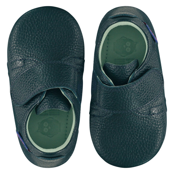 A pair of childrens adjustable strap shoes, viewed from the top. They are facing in opposite directions. They are in dark teal colour leather with a large adjustable strap over the top of the foot. They have a  pale blue leather lining and insole. The sole is a natural gum colour.