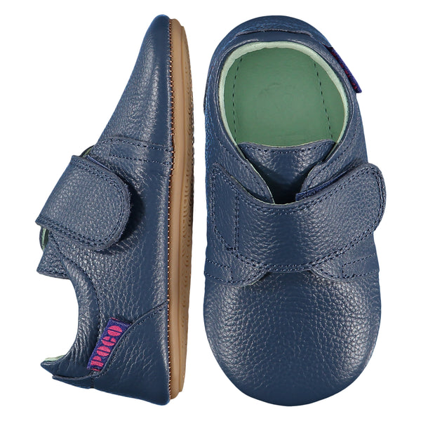 Mighty Shoes Navy Strap Shoe. Children's shoe in navy blue colour leather. Barefoot shoe with self fastening strap and a flat, super flexible TPU rubber sole. The sole has the Poco Nido logo on it. View of top and sole. Poco Nido baby, toddler and childrens shoes make unique gifts - as christmas gifts, stocking fillers, baby shower gifts, new parent gifts, to celebrate new walking skills and many other occasions. They are great toddler shoes too and are perfect for daycare settings.