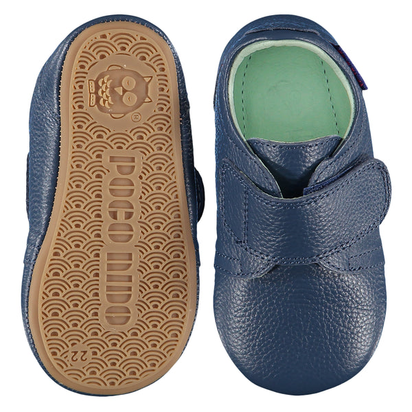 Mighty Shoes Navy Strap Shoe. Children's shoe in navy blue colour leather. Barefoot shoe with self fastening strap and a flat, super flexible TPU rubber sole. The sole has the Poco Nido logo on it. View of top and sole. Poco Nido baby, toddler and childrens shoes make unique gifts - as christmas gifts, stocking fillers, baby shower gifts, new parent gifts, to celebrate new walking skills and many other occasions. They are great toddler shoes too and are perfect for daycare settings.